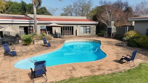 A swimming pool with a curved edge, surrounded by a patio with lounge chairs and a covered outdoor seating area.