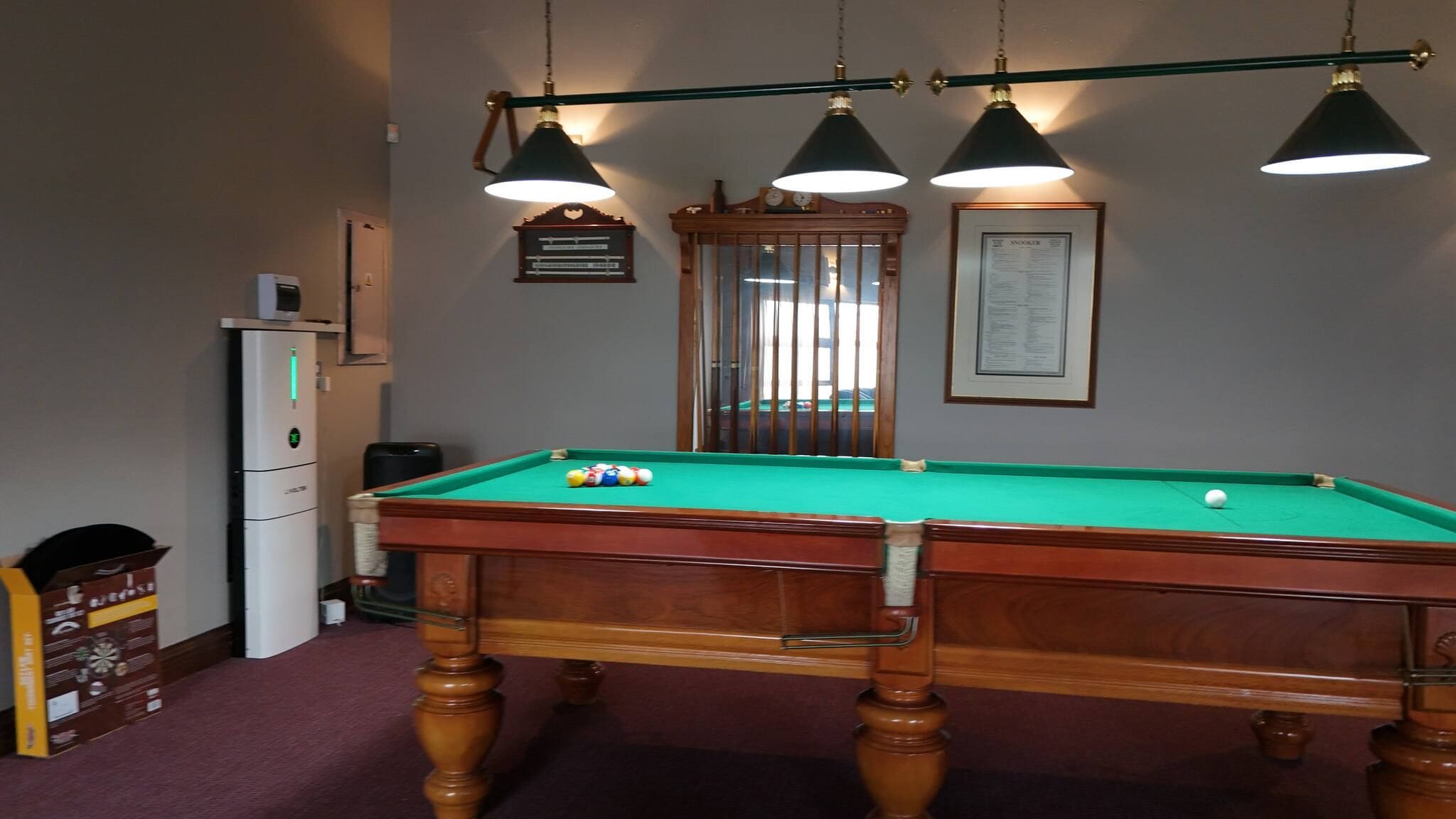 A pool table with balls, a clock, and a framed menu on the wall.