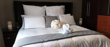 Un lit bien fait, avec une couette blanche, plusieurs oreillers et une serviette décorative.