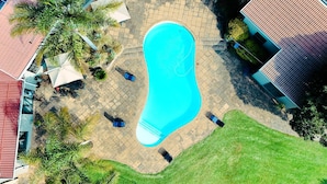 Een zwembad omringd door een terras met tuinmeubilair en palmbomen.