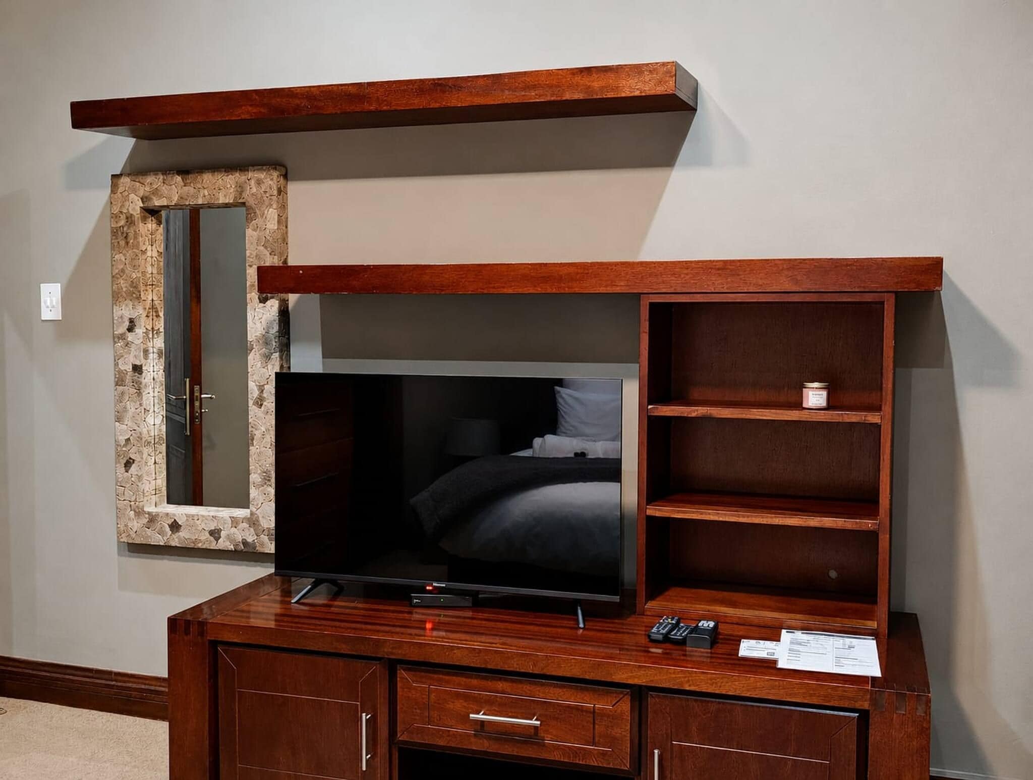 A wooden entertainment center with a flat-screen TV, a mirror, and built-in shelving.