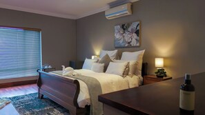Een slaapkamer met een bed, nachtkastjes, een airconditioning en een schilderij, plus een raam met zonwering.
