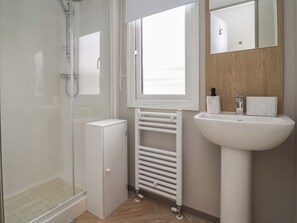 A bathroom with a glass shower enclosure, a white cabinet, a radiator, and a sink with a mirror above it. - Victory Festival (Abergele)