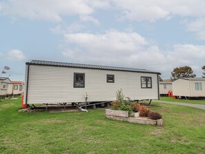 A mobile home with a flat roof, two windows, and a small garden area with plants. - Victory Festival (Abergele)