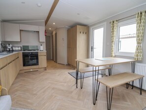 A modern kitchen with a dining area, wooden cabinets, and a window with curtains. - Victory Festival (Abergele)