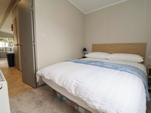A bedroom with a bed, a nightstand, a lamp, and a door leading to another room. - Victory Festival (Abergele)