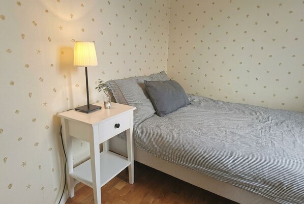 A bedroom with a bed, a bedside table with a lamp, and a wall with a pattern.