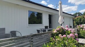 A white building with a large window, a patio with a table and chairs, and a wooden deck.
