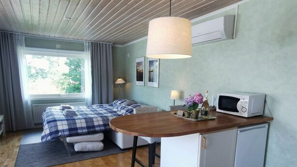 A compact room with a bed, a small kitchenette, a dining area, and a window with curtains.