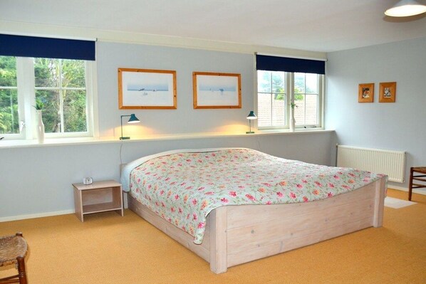 Ein Schlafzimmer mit einem Bett, zwei Nachttischen, einem Sessel und einem Fenster mit Vorhängen.