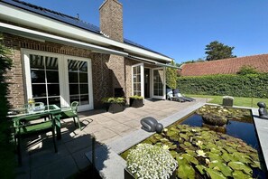 Ein Haus mit Terrasse, einem Teich mit Seerosen und einer Ziegel-Fassade.