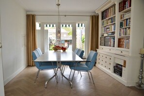 A dining area with a table and chairs, a bookshelf, and a view through a door. - Holiday apartment with 3 bedrooms (Castricum)