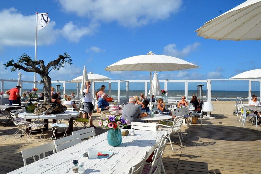 An outdoor dining area with tables and umbrellas, overlooking the sea.