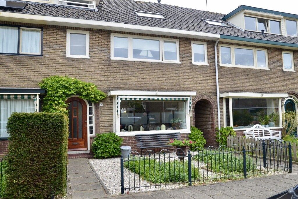 Een woonhuis met twee verdiepingen, een bakstenen gevel, meerdere ramen en een voortuin met een hek.