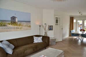 Un salon avec un canapé marron, une table basse, un tableau représentant un chalet de plage et un coin repas avec une table et des chaises.