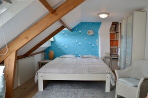 Une chambre avec un plafond en pente, un lit, une chaise, une bibliothèque et une horloge murale.