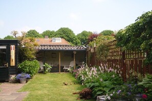 Un jardin avec une pelouse, une clôture en bois et une maison avec un toit en tuiles.
