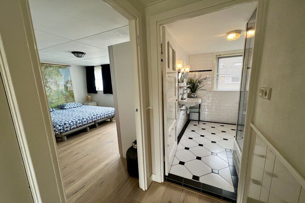 A room with a bed, a small kitchenette, and a bathroom with a tiled floor.