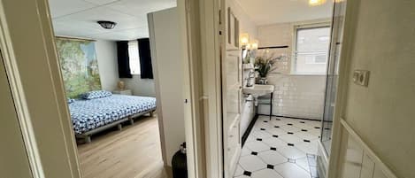 A room with a bed, a small kitchenette, and a bathroom with a tiled floor.