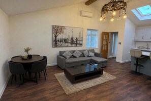 Una sala de estar moderna con un sofá seccional, una mesa de comedor con sillas, una mesa de centro y un cuadro de un paisaje urbano.