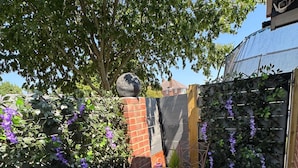Um pátio com duas mesas de mosaico, uma parede de tijolos e uma planta trepadeira com flores roxas.