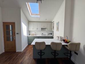 A modern kitchen with a skylight, a wooden door, and a bar area with three stools. - Luxury Flat With Parking & Underfloor Heating (Bournemouth)