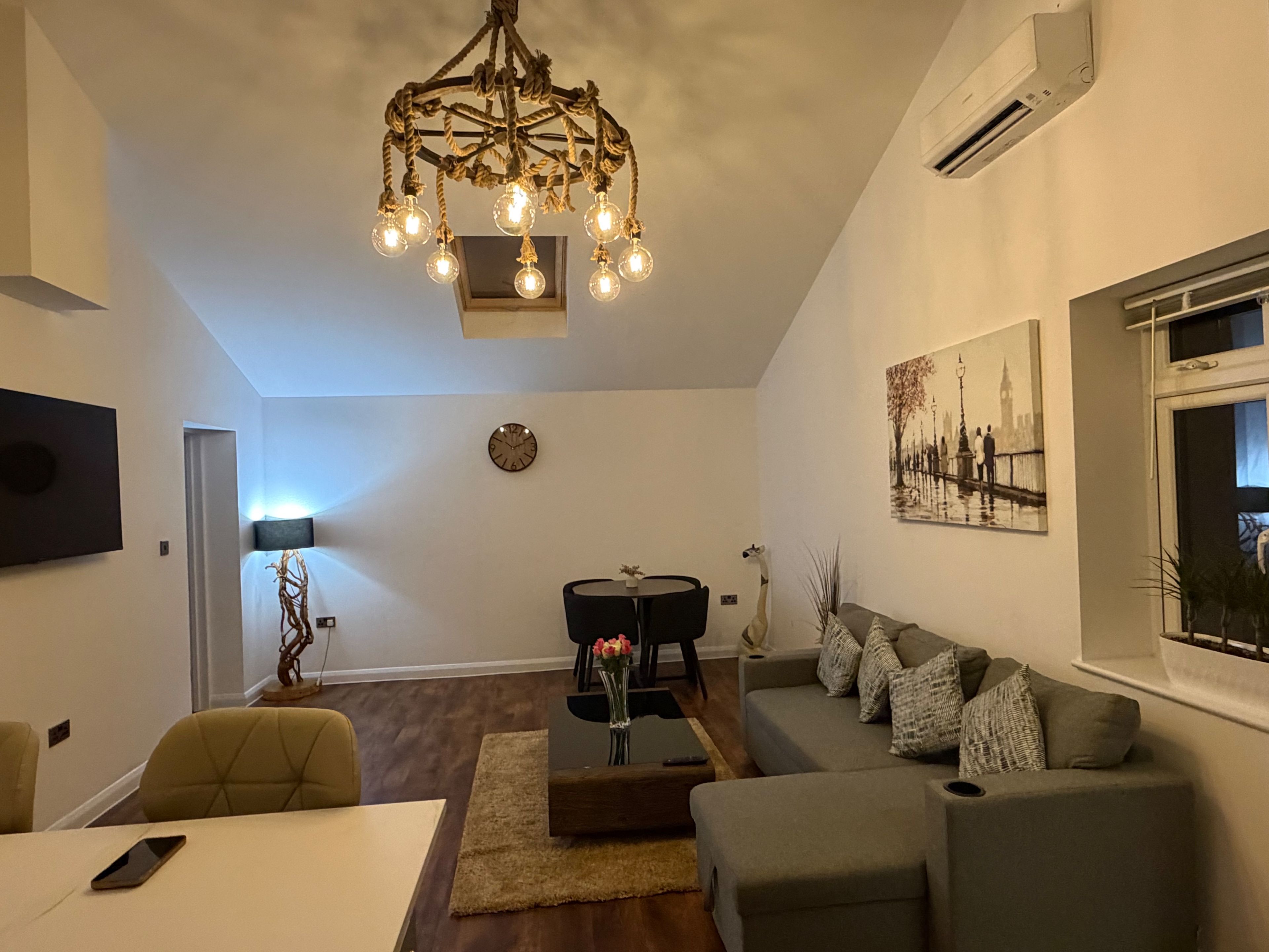 A modern living room with a chandelier, a sofa, a dining table, and a painting on the wall.