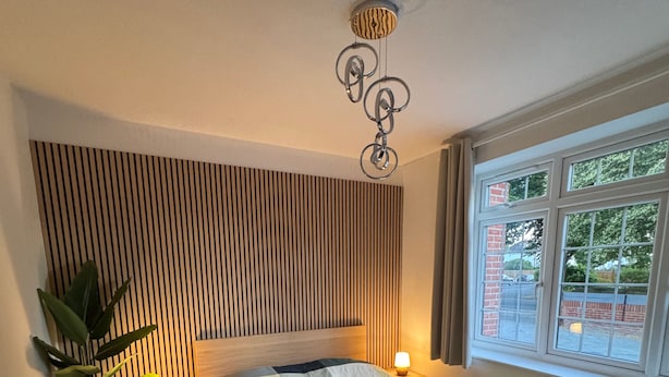 Quarto com cama, luminárias de cabeceira, planta em vaso e janela com vista.