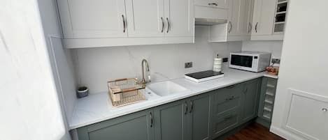 A modern kitchen with white cabinets, a stainless steel sink, and a microwave.