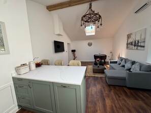 Una sala de estar moderna con un sofá gris, un comedor con una mesa blanca y una cocina con armarios verdes.