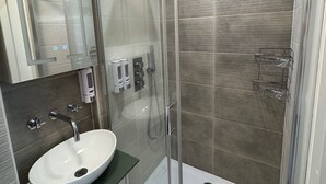 Uma casa de banho moderna com chuveiro envolto em vidro, lavatório branco e espelho sobre o lavatório.