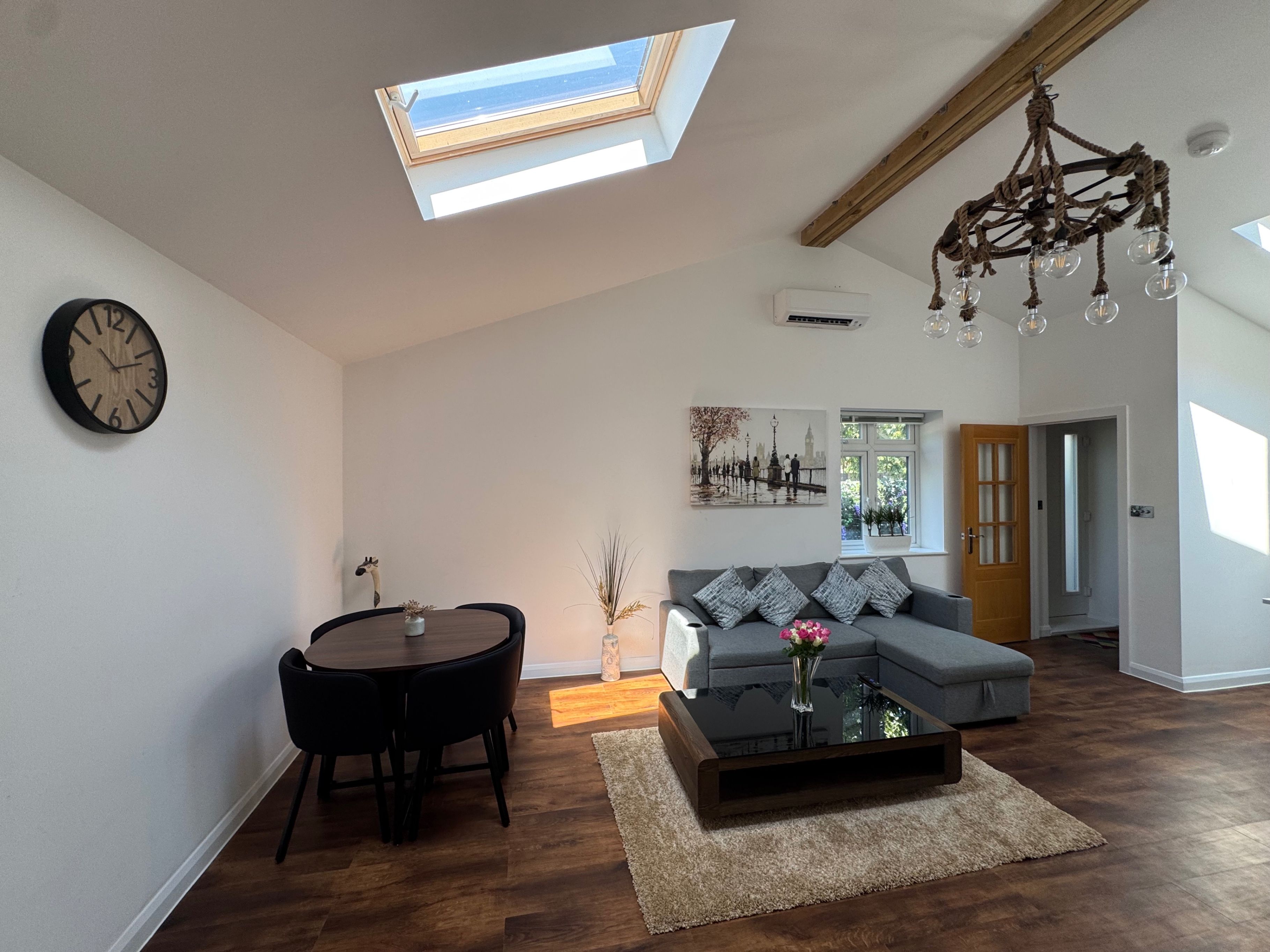 A modern living room with a skylight, a dining area with a round table, a sofa, and a decorative chandelier.