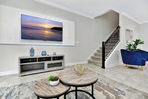 A modern living room with a flat-screen TV, a console table, two round tables, a staircase, and blue armchairs. - 1128 Cozy Townhouse/Near Disney/Free Water Park (Davenport)