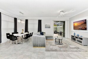 Ein modernes Wohnzimmer mit Essbereich, einem grauen Sofa, einem Couchtisch und einem großen Gemälde an der Wand.