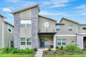 A modern two-story residential building with a stone accent wall, a blue door, and a small porch. - 1128 Cozy Townhouse/Near Disney/Free Water Park (Davenport)