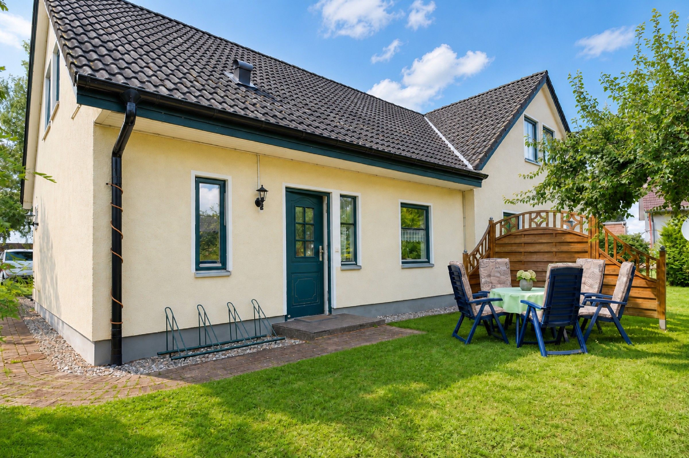 A two-story house with a tiled roof, a front door, and a small porch with outdoor furniture.