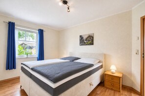 A bedroom with a bed, a nightstand, a painting, and a window with curtains. - Enjoy a relaxing stay at the Dück vacation rental on Rügen (Putbus)