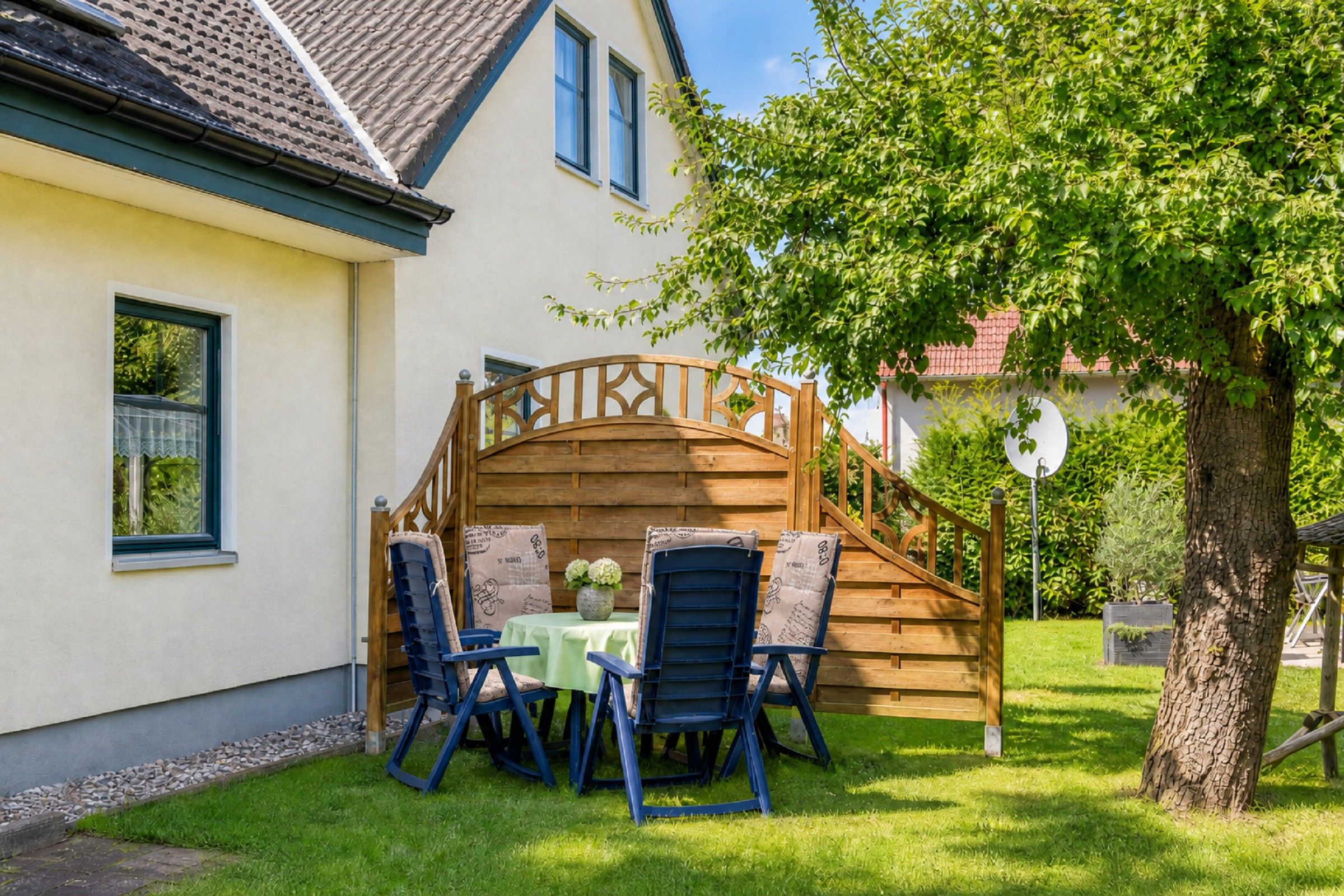 Eine Holzterrasse mit Tisch und Stühlen, eine Treppe und ein Baum in einer Wohngegend.