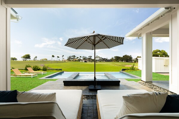 A pool area with lounge chairs and an umbrella, overlooking a grassy lawn and houses. - Hale Olina by Alekona Kauai (Koloa)