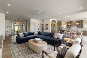 Ein geräumiges Wohnzimmer mit einem Ecksofa, einem Couchtisch und einem Essbereich, im Hintergrund ist eine Küche zu sehen.