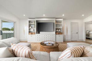 A living room with a large flat-screen TV, white cabinetry, and two surfboards. - Hale Olina by Alekona Kauai (Koloa)