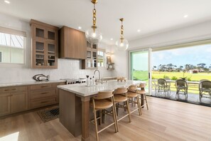 Een moderne keuken met houten kastjes, een centraal eiland met barkrukken en uitzicht op een groen landschap door de schuifpui.
