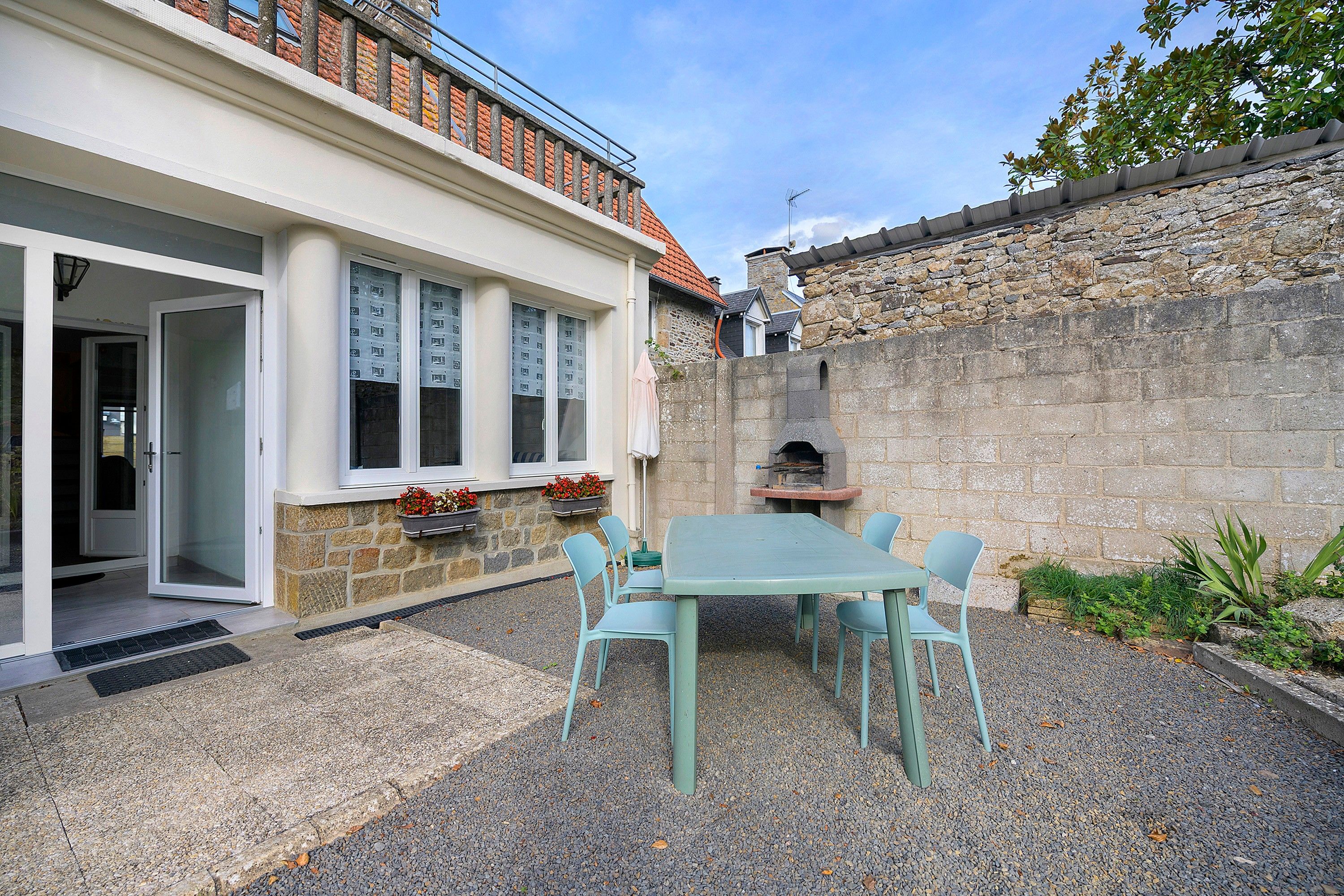 Eine Terrasse mit Tisch und Stühlen, eine Steinmauer und ein Gebäude mit einem Ziegeldach.