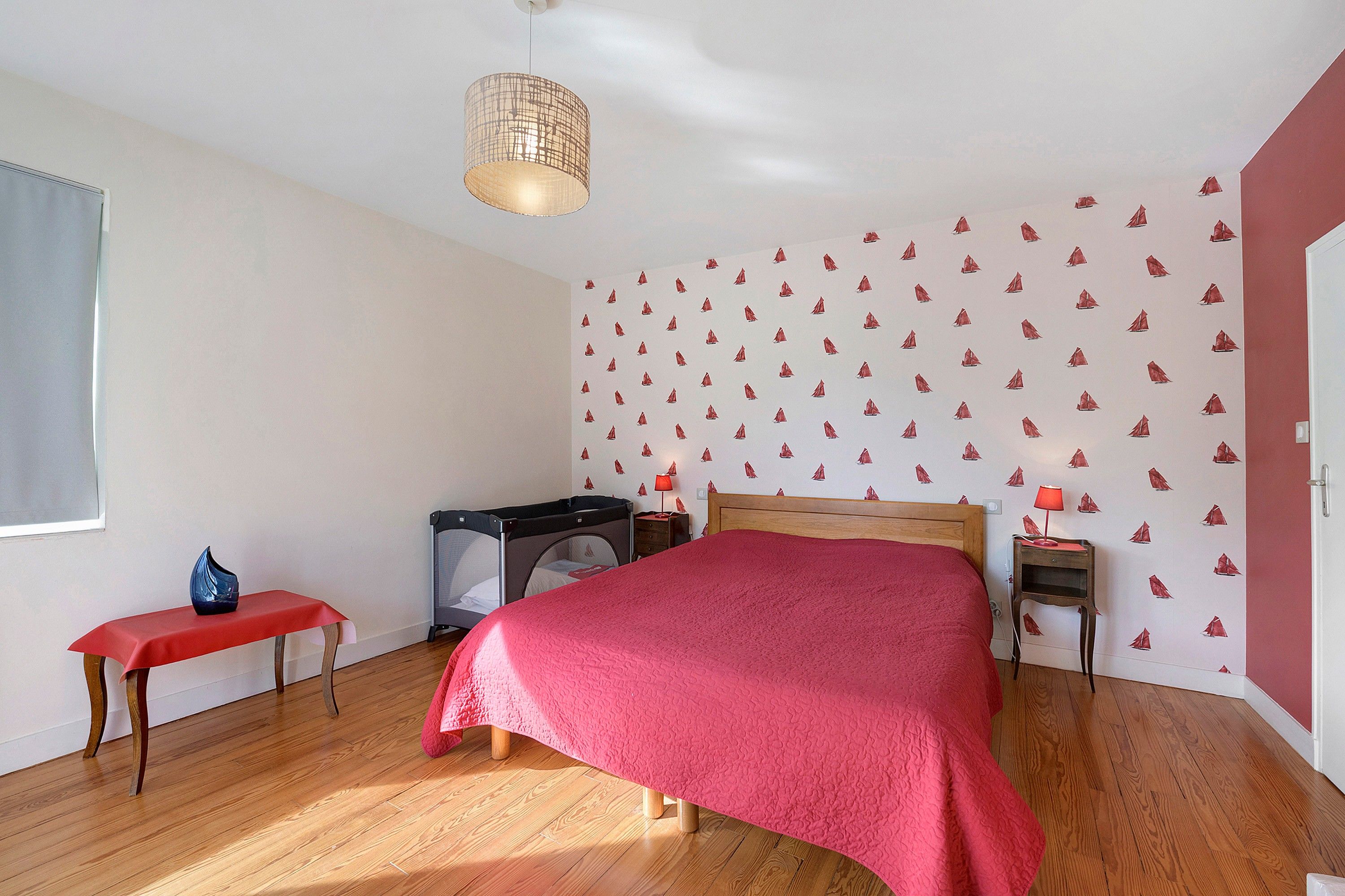 A bedroom with a bed, a desk, a chair, a lamp, and a window.