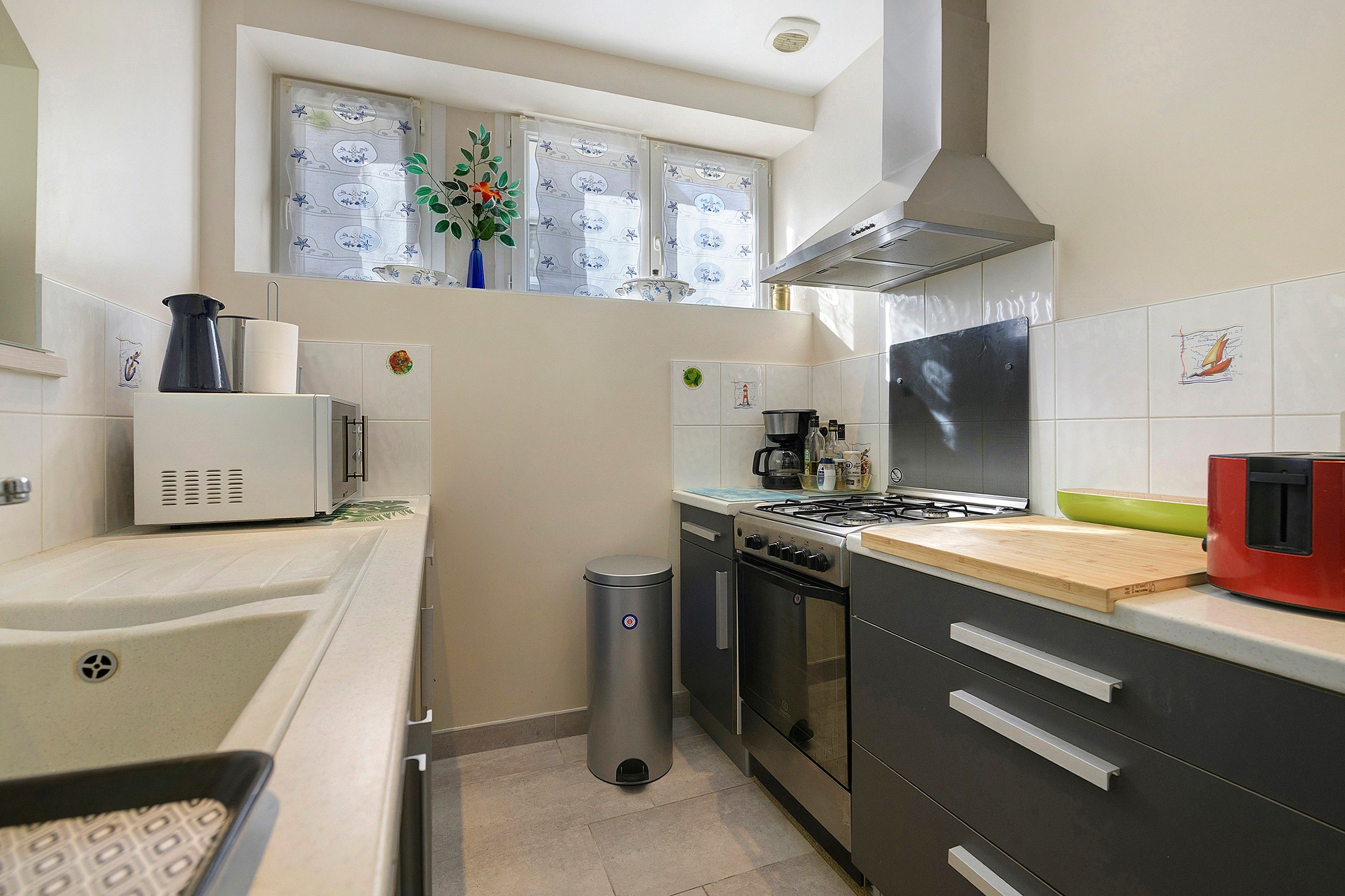 A compact kitchen with a gas stove, a microwave, and a trash bin.