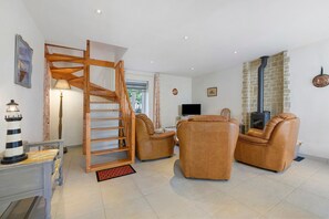 A living room with a wooden spiral staircase, leather sofas, a television, and a fireplace.