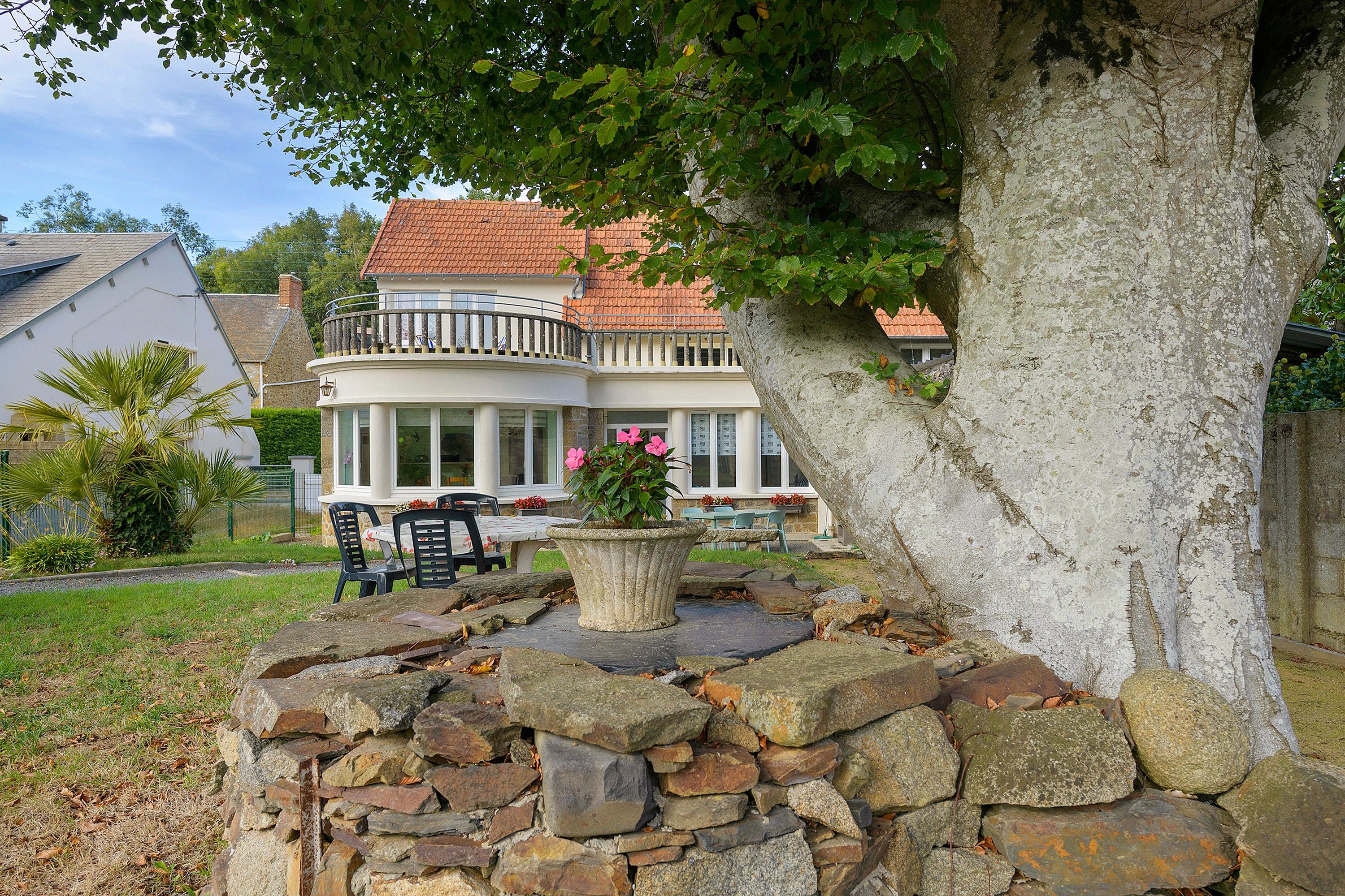 A house with a stone wall, a balcony, and a tree.