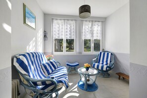 A sunlit room with two blue-striped armchairs, a small round table with a vase, and a bench.