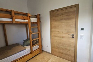 Un lit superposé avec une échelle, une porte en bois et un interrupteur sur le mur.