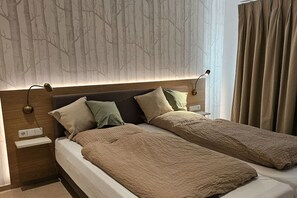 A double bed with a textured blanket, a nightstand with a lamp, and a wall with a tree pattern.